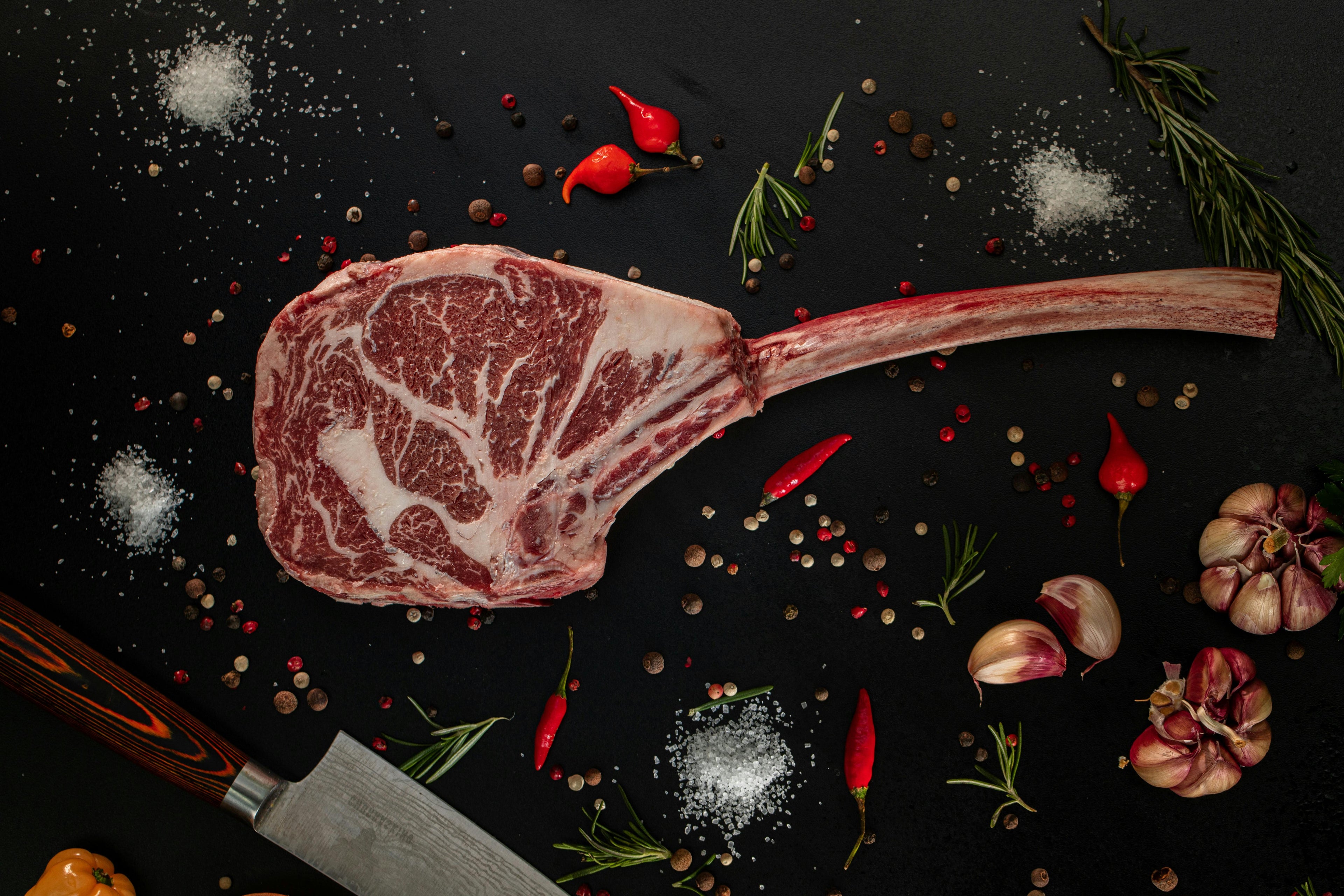 Raw tomahawk beef steak with marbling and spices on dark background